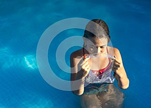 Cute young well tanned girl in the swimming pool holding her diving mask. Copy space.