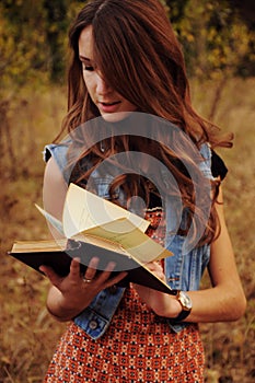 Cute young woman in the autumn forest reading a book