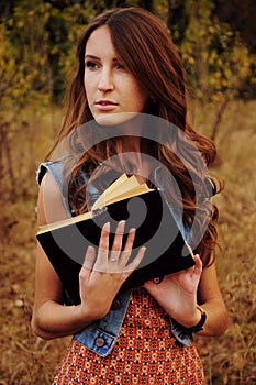 Cute young woman in the autumn forest reading a book