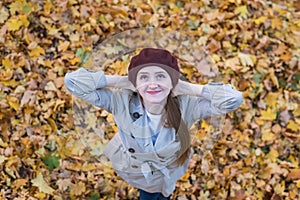 Cute young woman in beret on yellow autumn leaves background. Top view