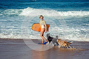 Cute young woman bodyboarding in swimsuit with her dogs