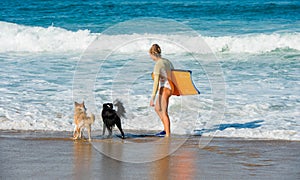 Cute young woman bodyboarding in swimsuit with her dogs
