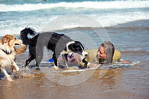 Cute young woman bodyboarding in swimsuit with her dogs