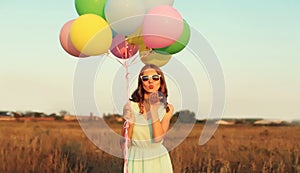Cute young woman with bunch of colorful balloons outdoors in field