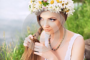 Cute young woman with circlet of camomile braiding her hair at t