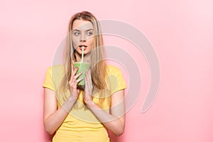 Cute young woman drinking a green smoothie and thinking about healthy nutrition detox food.