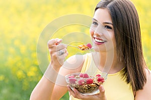 Cute young woman eating healthy cereals outdoors.