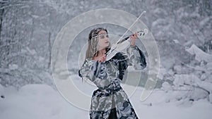 Cute young woman in fairy tale image in grey royal dress plays white violin on snow