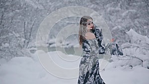Cute young woman in fairy tale image in grey royal dress stands in snow
