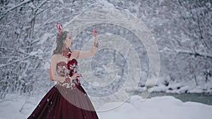 Cute young woman in fairy tale image in red royal dress stands in snow