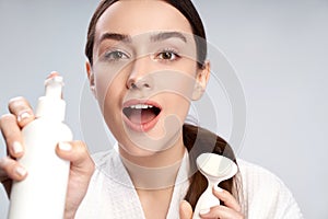 Cute young woman holding bottle of cosmetic cream and pore cleansing brush