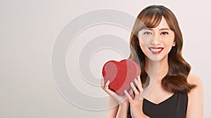 Cute young woman holding pink heart symbol against pale white background