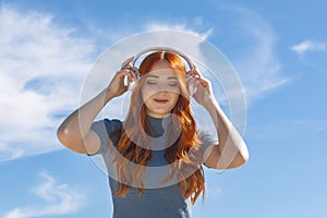 Cute young woman listening to music with wireless headphones and looking down with the sky in the background and copy