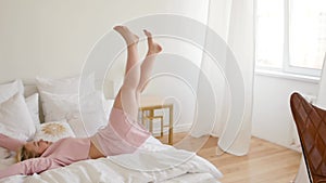 Cute young woman in pink pajamas has fun jumping on her bed