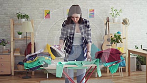 Cute young woman in plaid shirt ironing laundry iron