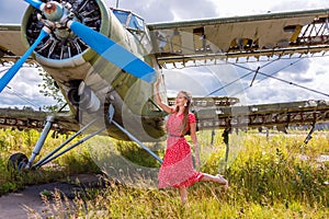Cute young woman in a red pin up style dress standing by an abandoned green plane