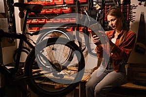 Cute young woman repairing a broken bicycle with tools and technology working in her garage. Female cyclist thoroughly