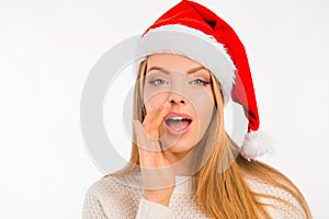 Cute young woman with santa`s hat tells the news holds hand near mouth