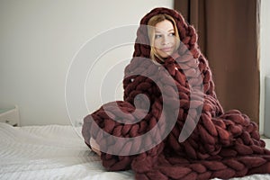 Cute young woman is sitting on the bed wrapped in a big and fluffy brown plaid. Warmth and comfort of home photo