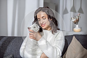Cute young woman sitting on the sofa and hugging her cat