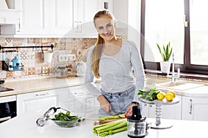 A cute young woman is slicing vegetables in the kitchen and preparing the ingredients for a green smoothie. Healthy