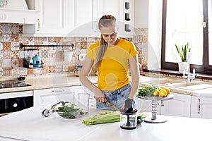 A cute young woman is slicing vegetables in the kitchen and preparing the ingredients for a green smoothie. Healthy