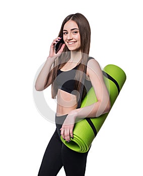 Cute young woman in sportswear with green mat ready for workout. Smiling and talking on the phone. Isolated on white background.