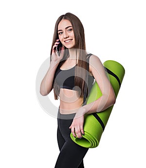 Cute young woman in sportswear with green mat ready for workout. Smiling and talking on the phone. Isolated on white background.