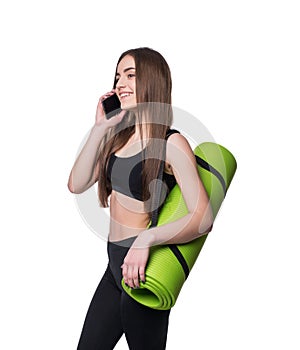 Cute young woman in sportswear with green mat ready for workout. Smiling and talking on the phone. Isolated on white background.