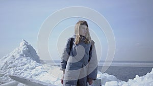 Cute young woman in warm jacket walking on the glacier, holding her cellphone in raised hand, trying to find mobile