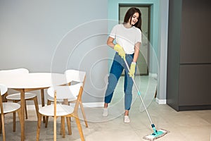 Cute young woman in yellow gloves doing cleaning washing kitchen floor