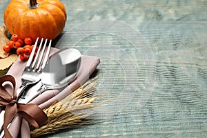 Cutlery with napkin, wheat spikes and pumpkin on blue wooden table, space for text. Thanksgiving Day