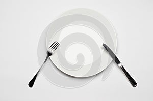 Cutlery and restaurant topic: Fork knife and white plate lying on a white table isolated in the studio top view