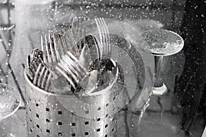 Cutlery spoons and forks, glasses and plates under running water in the dishwasher