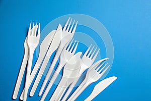 Cutlery, white plastic knives and forks. Disposable plastic tableware on blue background, top view