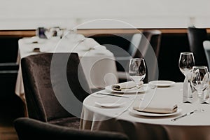 Cutlery and wine Glasses on white tablecloth, empty armchairs near. Banquet hall in restaurant. Served table for guests in cafe. C