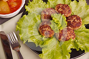 Cutlets and lettuce leaves on a black plate and cutlery.