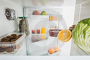 Cutlets with ripe fruits and cabbage in refrigerator with open door  on white