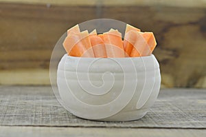 Cuts stick of carrot in bowl on wooden background