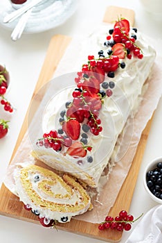 Cutted sponge biscuit cake roll filling whipped cream and berries decorated strawberry, blueberry and red currants on white