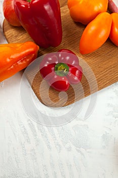 Cutting board with assort of different tomatoes and bell pepper on white wooden background