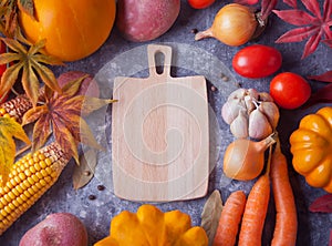 Cutting board, autumn leaves, vegetables on the black background. Autumn harvest. Autumn food. Top view. Copy space