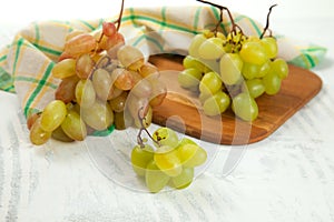 Cutting board with bunch of organic green and pink grapes on white wooden background