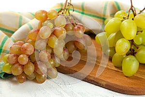 Cutting board with bunch of organic green and pink grapes on white wooden background
