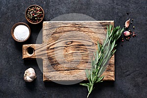 Cutting board with fresh rosemary and spices on a black concrete table. Top view with copy space