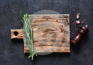 Cutting board with fresh rosemary and spices on a black concrete table. Top view with copy space
