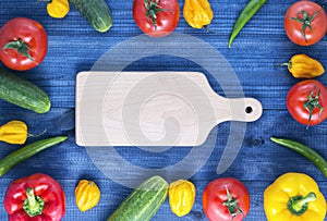 Cutting board and fresh vegetables on wooden table. red and yellow peppers, cucumber chilli and habanero peppers, tomatoes.