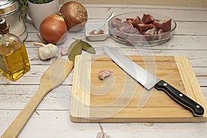 A cutting board with a knife and the ingredients to make a goulash stew.