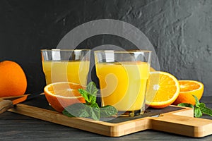 Cutting board with orange juice, mint, knife and oranges on wooden table against black background, space for text