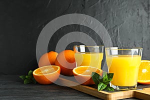 Cutting board with orange juice, mint and oranges on wooden table against black background, space for text